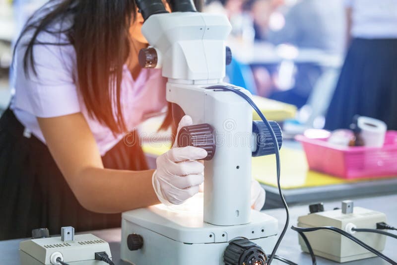 Student girl looking through microscope in science laboratory