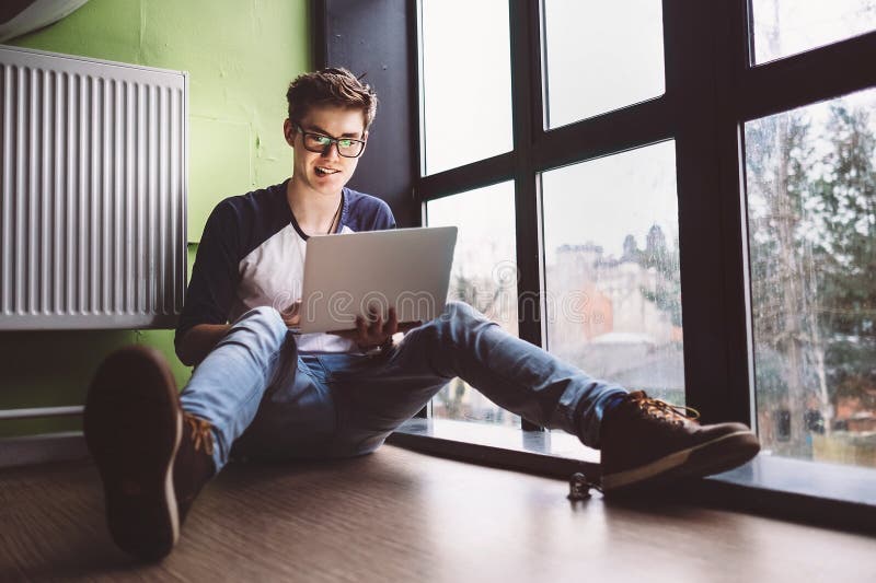Student het werken met laptop zit op de vloer dichtbij het venster stock afbeelding Student het werken met laptop zit op de vloer dichtbij het venster stock afbeelding