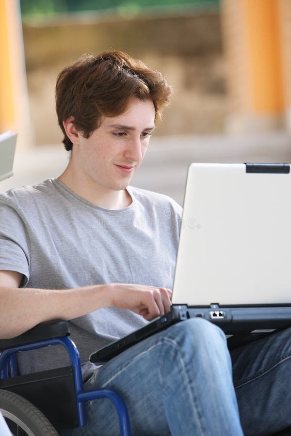 Disabled young man sitting in wheelchair using laptop. Disabled young man sitting in wheelchair using laptop