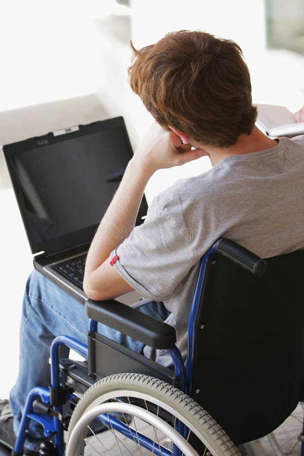 Disabled young man sitting in wheelchair using laptop. Disabled young man sitting in wheelchair using laptop