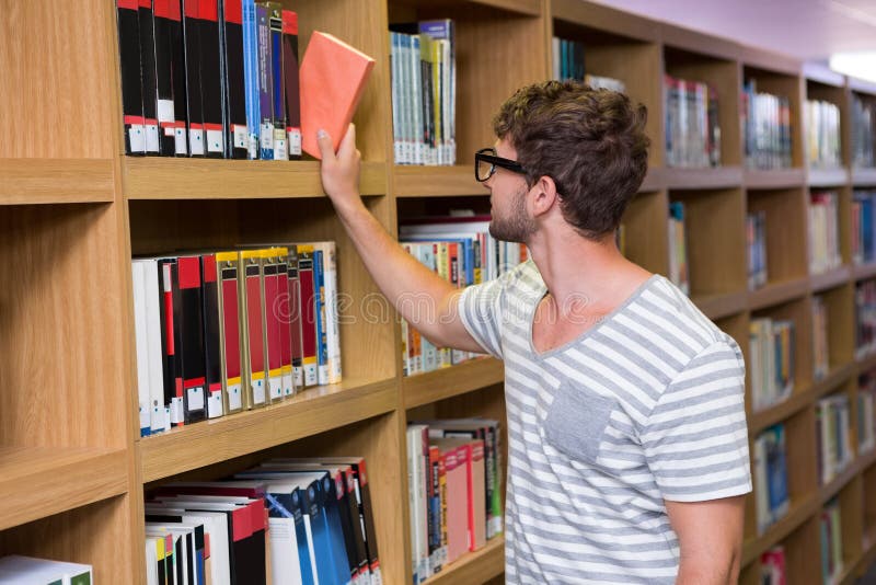 Мужчина в библиотеке. Студент у книжной полки. Мужчина у книжной полки. Выбирает книгу.