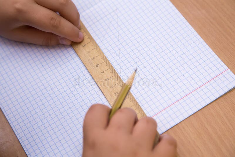 The student pressed a ruler to a notebook sheet, a pencil in his hand. stock photo