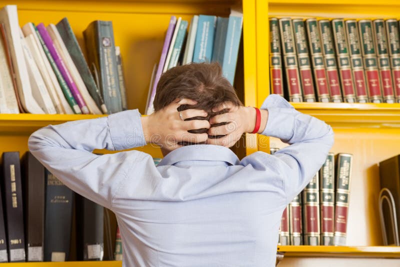 Student Pulling Hair Against Bookshelf In stock photos