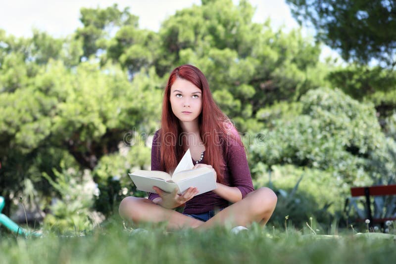 Student sitting in the park with a book looking up