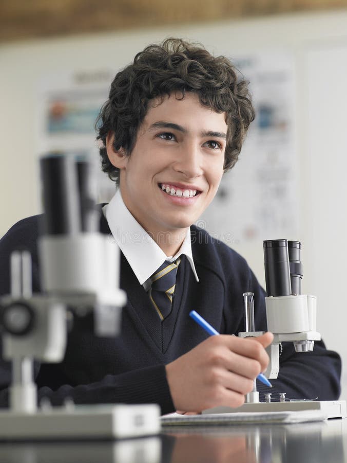 High school student using microscope and taking notes in classroom