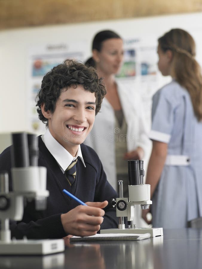 Portrait of high school student using microscope and taking notes in laboratory