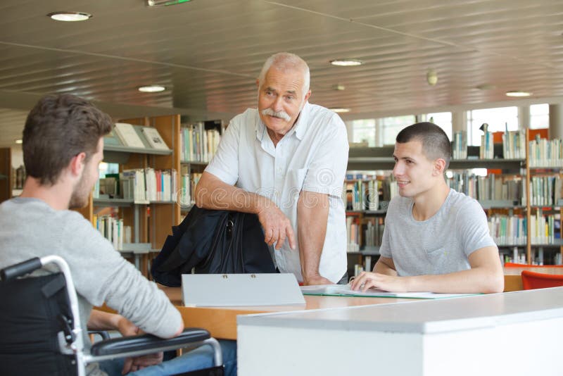 Student in wheelchair talking to libarian and friend in library royalty free stock photos