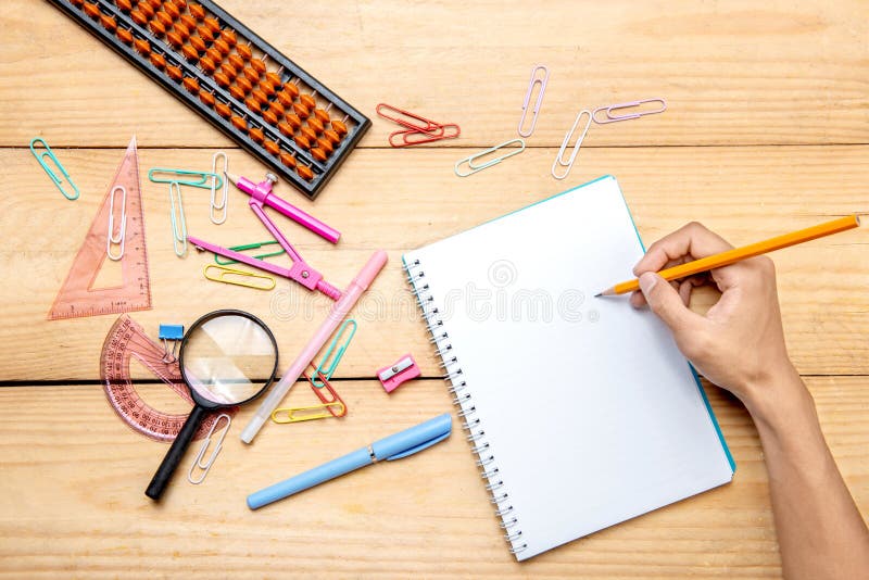 Student writing in notebook with school supplies and stationery on the wooden table