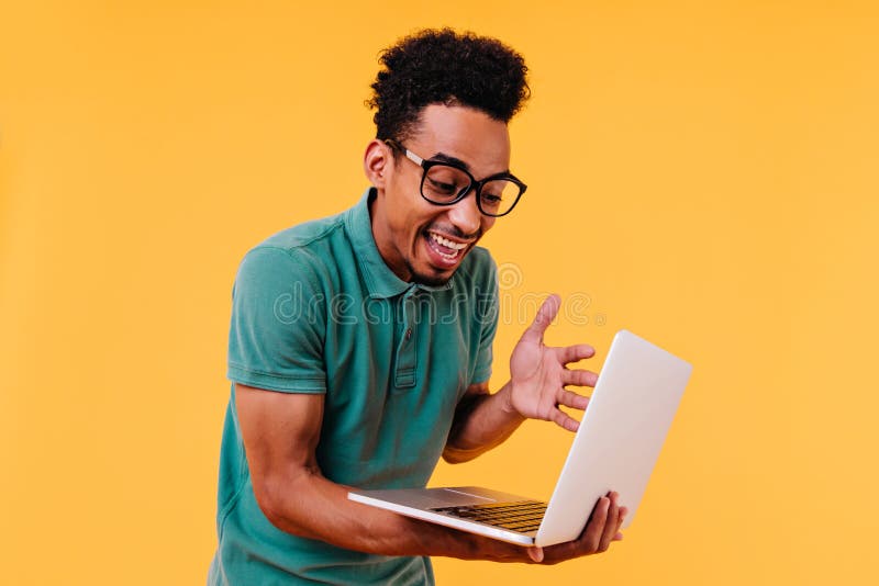 Studente di sesso maschile sorpreso che guarda lo schermo del portatile. foto di freelancer africano in interni portano dei vetri fotografia stock