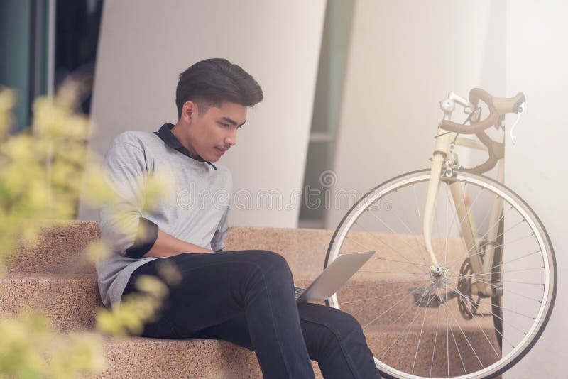 Studente maschio asiatico che si siede alle scale e che sorride come lapt di uso fotografia stock libera da diritti Studente maschio asiatico che si siede alle scale e che sorride come lapt di uso fotografia stock libera da diritti