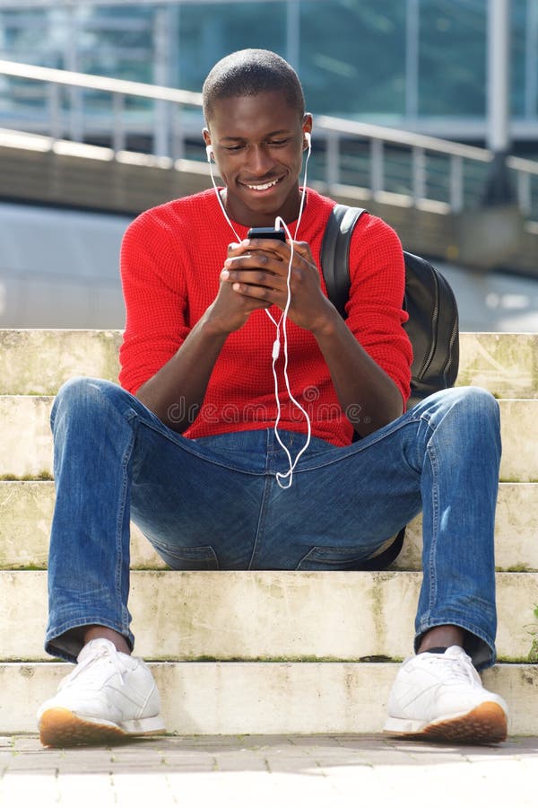 Studente maschio nero che si siedono all'aperto e musica d'ascolto fotografia stock libera da diritti Studente maschio nero che si siedono all'aperto e musica d'ascolto fotografia stock libera da diritti