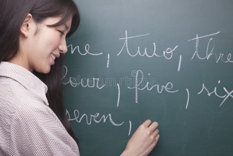 Studente sorridente della giovane donna che scrive i numeri inglesi sulla lavagna immagini stock Studente sorridente della giovane donna che scrive i numeri inglesi sulla lavagna immagini stock