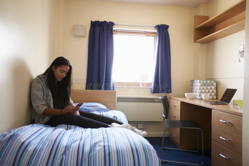 Student Uses Mobile Phone In Bedroom Of Campus Accommodation. Student Uses Mobile Phone In Bedroom Of Campus Accommodation