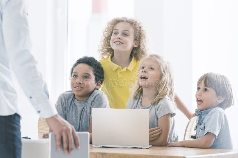 Happy, curious elementary school students admiring their computer science teacher talking about programming. Happy, curious elementary school students admiring their computer science teacher talking about programming