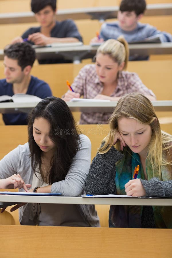 Studenten, die in einem Vorlesungssal mit einem Mädchen verwendet Tabletten-PC lernen lizenzfreie stockbilder Studenten, die in einem Vorlesungssal mit einem Mädchen verwendet Tabletten-PC lernen lizenzfreie stockbilder