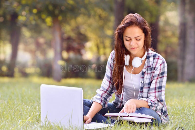 Studentenmädchen, das an dem Laptop, sitzend auf Gras im Park arbeitet lizenzfreies stockbild Studentenmädchen, das an dem Laptop, sitzend auf Gras im Park arbeitet lizenzfreies stockbild