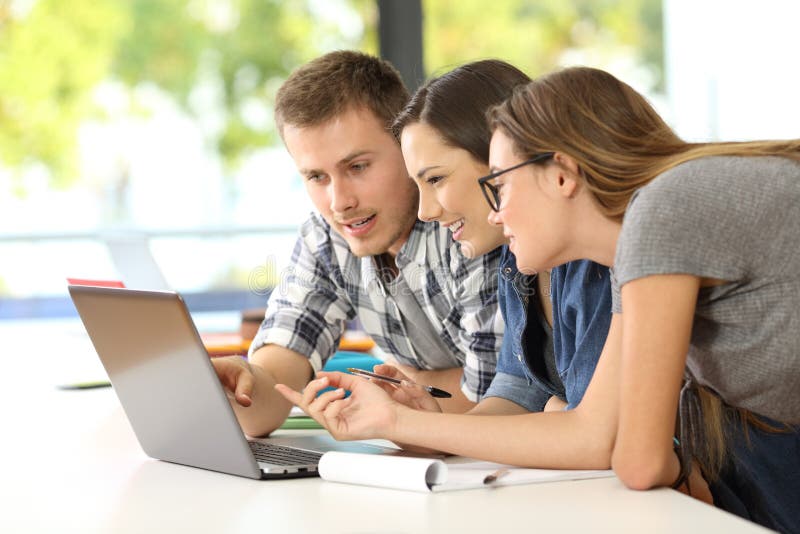 Three students learning together on line with a laptop in a classroom. Three students learning together on line with a laptop in a classroom