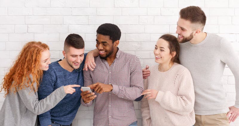 Students watching funny content on phone, guy showing new video over white wall. Students watching funny content on phone, guy showing new video over white wall