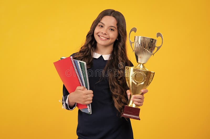Studentessa vincitrice del trofeo. Libri per bambini con trofeo d'oro o coppa vincente isolata in giallo fotografie stock