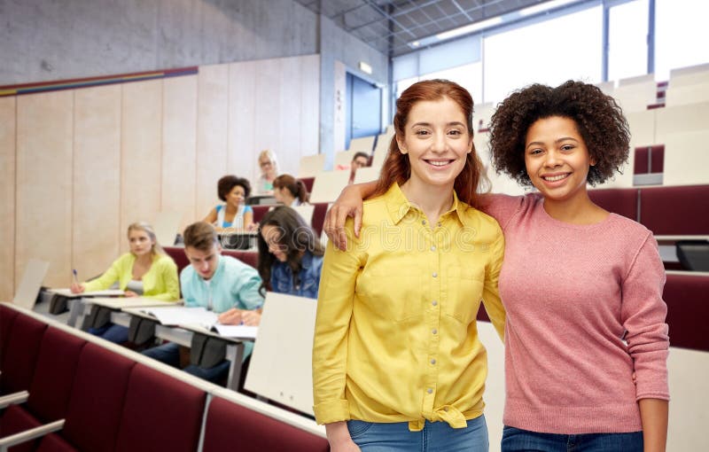 Studentesse felici che sorridono abbracciate all'università fotografia stock