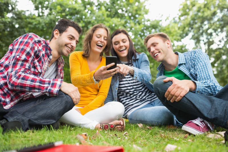 Studenti di college felici che esaminano telefono cellulare in parco immagini stock libere da diritti Studenti di college felici che esaminano telefono cellulare in parco immagini stock libere da diritti
