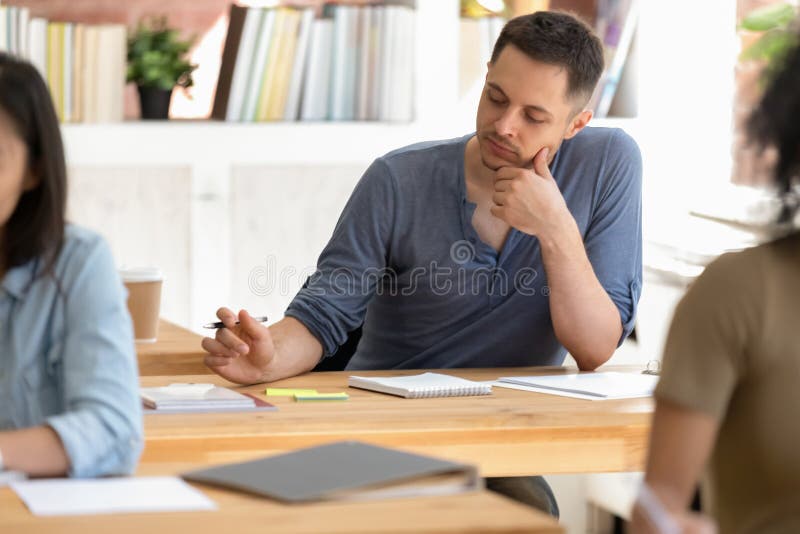 Students sitting at desks focus on caucasian guy make notes stock photography