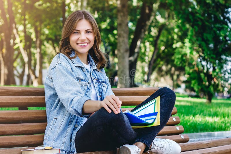 Studentă care stă pe o bancă în parc cu carnete și dosare stock photo