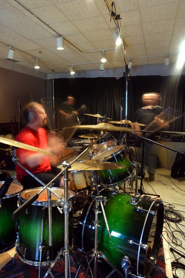 A bass player, guitar player and drummer recording tracks in a recording studio. Slow shutter speed with ambient light - players have motion blur from slow shutter speed. A bass player, guitar player and drummer recording tracks in a recording studio. Slow shutter speed with ambient light - players have motion blur from slow shutter speed.