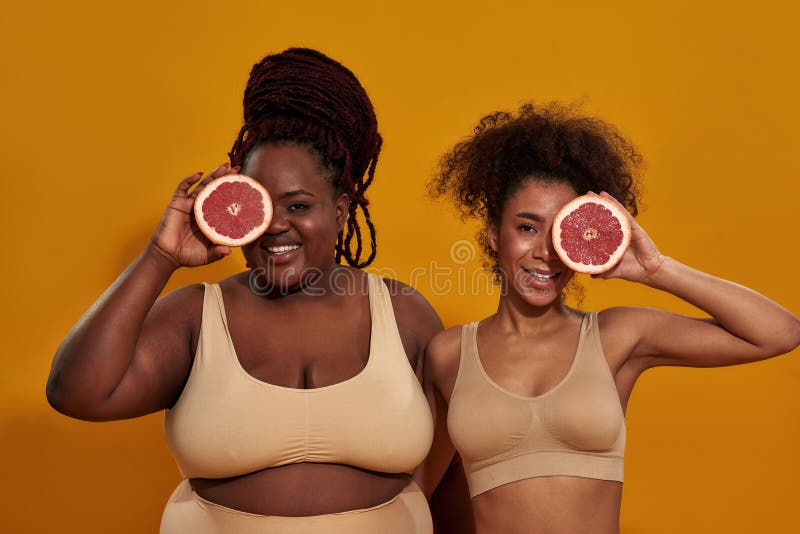 Studio-Aufnahme von zwei fröhlichen afrikanisch-amerikanischen Frauen in Unterwäsche lächelnd vor der Kamera, die ein Auge mit ein lizenzfreie stockfotografie