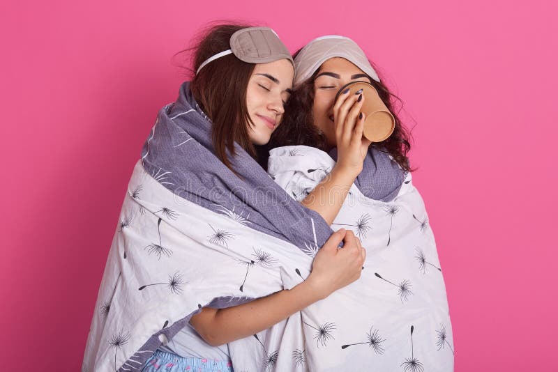 Studio die van vrouw het drinken koffie wordt geschoten terwijl haar vriend met gesloten eues haar tijdens pyjama'spartij koester royalty-vrije stock afbeeldingen Studio die van vrouw het drinken koffie wordt geschoten terwijl haar vriend met gesloten eues haar tijdens pyjama'spartij koester royalty-vrije stock afbeeldingen