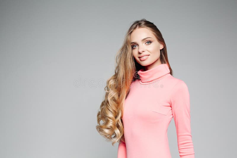 Studio portrait of a beautiful business woman blond with blue eyes with long hair, wears an elegant pink dress and holds