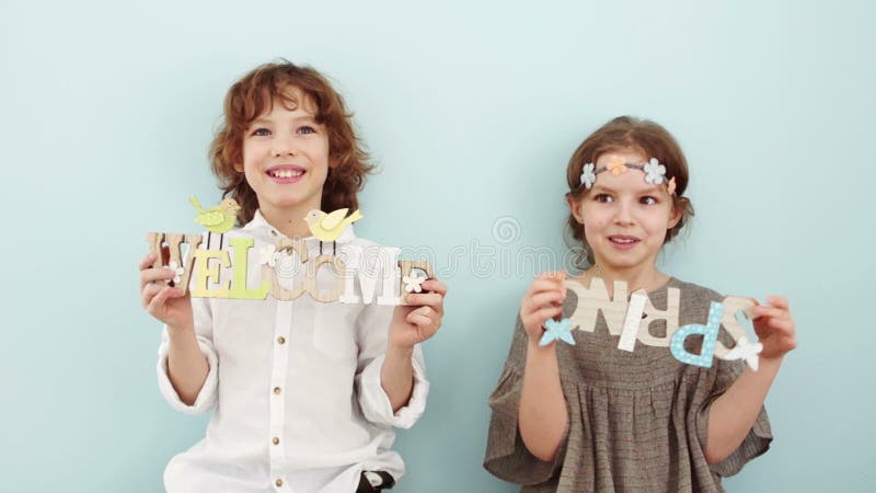 Studio portrait of cute school children with wooden signs. Spring holidays, pastel colors. The boy is wearing a white