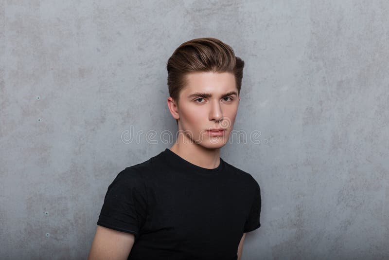 Studio portrait of a fashion young man with clean skin with a pierced nose with a trendy hairstyle in a stylish black t-shirt on a