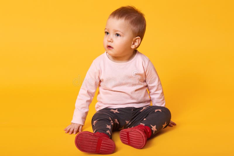 Studio shot of adorable little baby girl sitting on floor, isolated on yellow background, lovely baby portrait wearing casual stock images Studio shot of adorable little baby girl sitting on floor, isolated on yellow background, lovely baby portrait wearing casual stock images