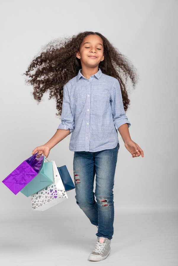 Studio shot of attractive little girl of mulatta with long frizzy. She has fun with paper bags from shopping, eyes closed from royalty free stock photo Studio shot of attractive little girl of mulatta with long frizzy. She has fun with paper bags from shopping, eyes closed from royalty free stock photo