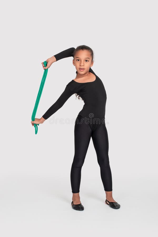 Studio shot of attractive little gymnast girl of mulatto with long braid of frizzy wearing black legends and a bathing suit