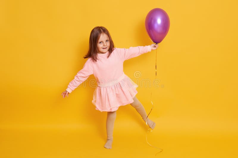 Studio shot of beautiful little girl wih bright purple balloon in hands, child standing on one hand isolated over yellow studio stock photo Studio shot of beautiful little girl wih bright purple balloon in hands, child standing on one hand isolated over yellow studio stock photo