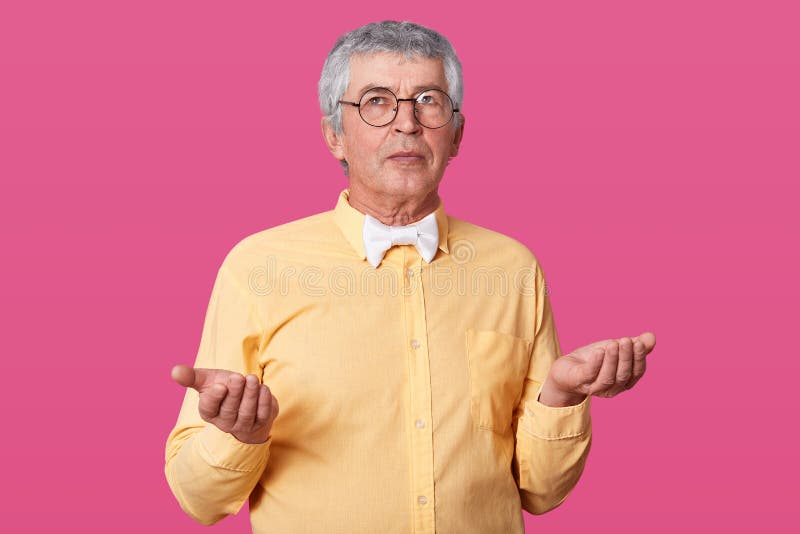 Studio shot of handsome old man wearing yellow shirt, white bow tie, and glasses, has serious facial expression, fells royalty free stock photos Studio shot of handsome old man wearing yellow shirt, white bow tie, and glasses, has serious facial expression, fells royalty free stock photos