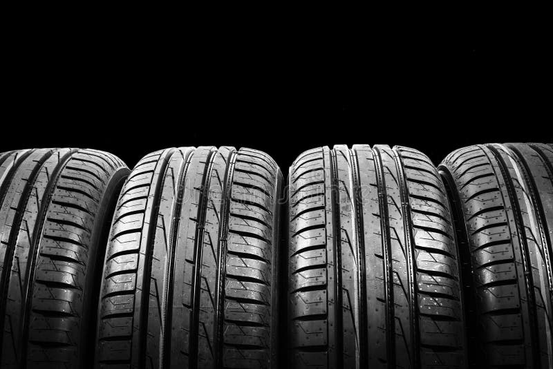 Studio shot of a set of summer car tires isolated on black background. Tire stack background. Car tyre protector close up. Black r