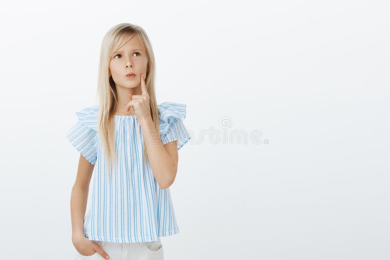 Studio shot of smart young girl with blond hair, looking up and holding finger on lip, frowning while thinking, making royalty free stock photos Studio shot of smart young girl with blond hair, looking up and holding finger on lip, frowning while thinking, making royalty free stock photos