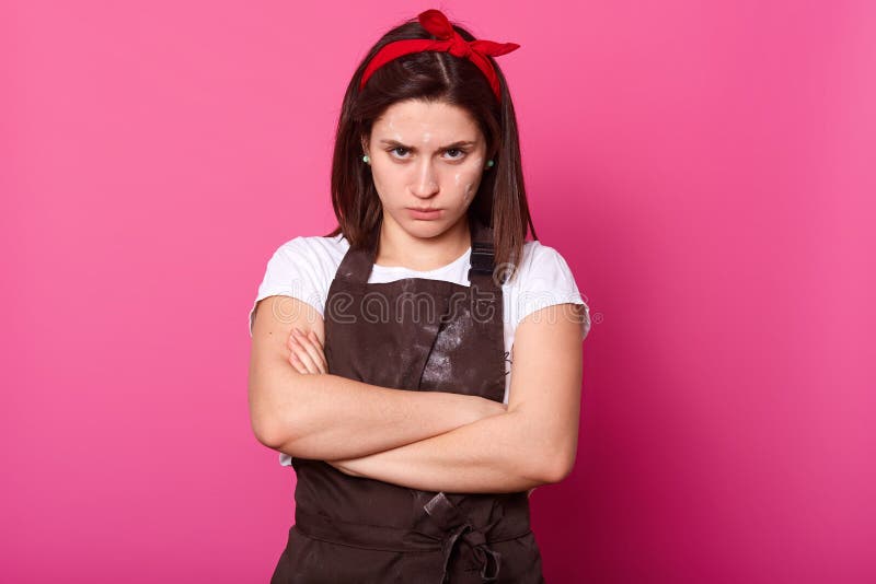 Studio shot of upset Caucasian housewife standing with arms folded, looks offended, wearing t shirt, apron and hair band, isolated royalty free stock photos Studio shot of upset Caucasian housewife standing with arms folded, looks offended, wearing t shirt, apron and hair band, isolated royalty free stock photos