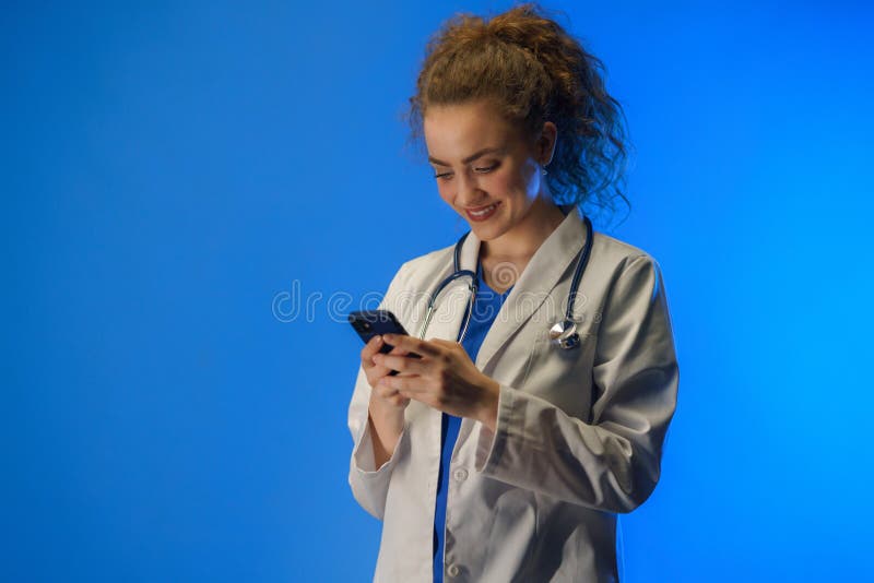 Studio Shot of a Young Female Doctor Using Mobile Phone Against a Blue