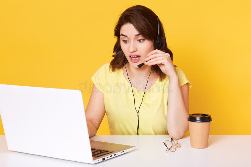 Studio sparato di giovane donna castana con la cuffia avricolare ed il microfono, lavorando come operatore con il computer portat fotografia stock Studio sparato di giovane donna castana con la cuffia avricolare ed il microfono, lavorando come operatore con il computer portat fotografia stock