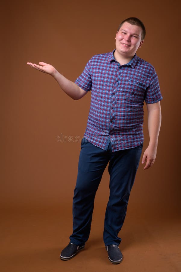 Studio van de te zware jonge mens tegen bruine achtergrond wordt geschoten die stock foto Studio van de te zware jonge mens tegen bruine achtergrond wordt geschoten die stock foto