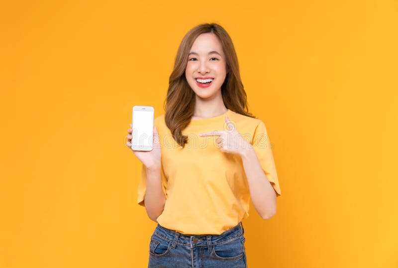 Studio zdjęcie pięknej azjatyckiej kobiety trzymającej smartfon i uśmiechającej się na jasnożółtym tle zdjęcie royalty free