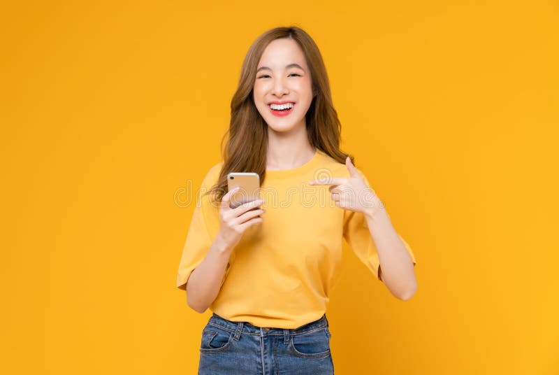 Studio zdjęcie pięknej azjatyckiej kobiety trzymającej smartfon i uśmiechającej się na jasnożółtym tle obrazy stock