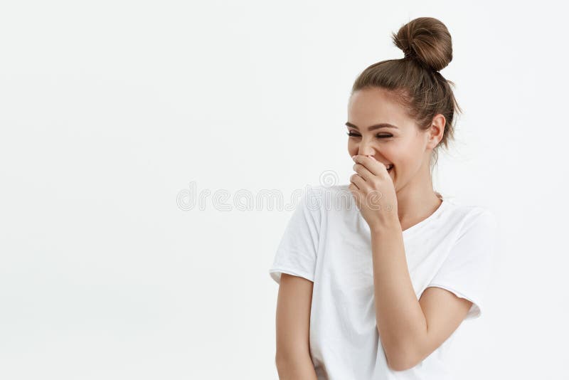 Studio portrait of playful feminine caucasian woman laughing while looking at copy space and covering mouth with hand, standing over white background. Elegant visagist talks with customer. Studio portrait of playful feminine caucasian woman laughing while looking at copy space and covering mouth with hand, standing over white background. Elegant visagist talks with customer.