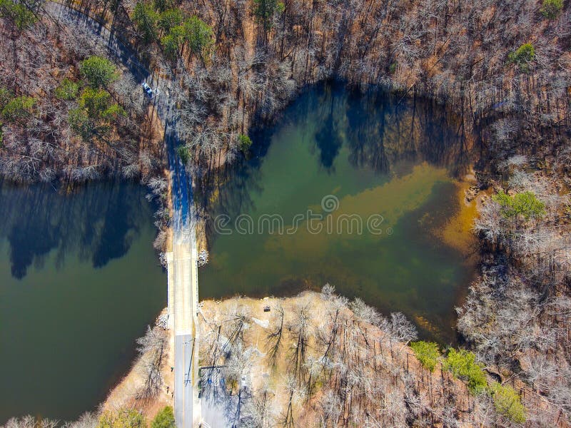 a stunning aerial shot of the deep green water and a bridge over the lake with lush green and autumn colored trees