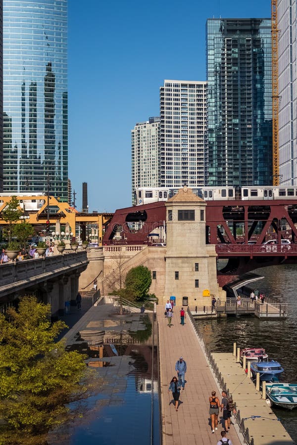 Stunning and colorful view of two el trains crossing the Chicago River and Wacker Dr. while commuters walk on riverwalk next to stock images Stunning and colorful view of two el trains crossing the Chicago River and Wacker Dr. while commuters walk on riverwalk next to stock images