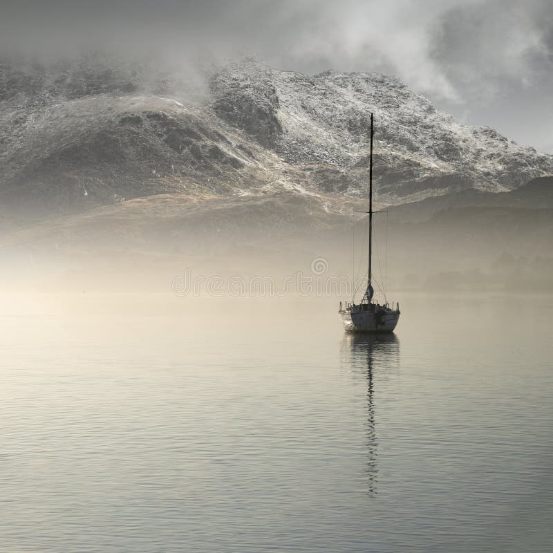 Stunning landscape image of sailing yacht sitting still in calm lake water with mountain looming in background during Autumn Fall
